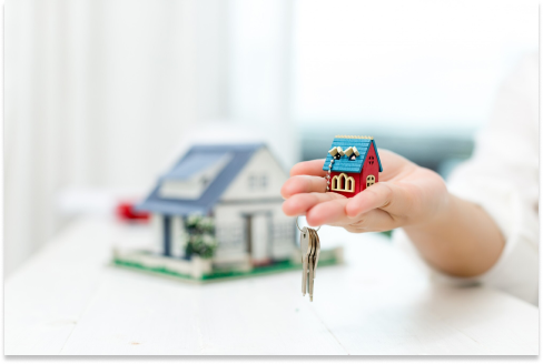 Mano entregando una llave frente a una casa pequeña - Arrendamientos JYA Inmobiliaria en Pasto